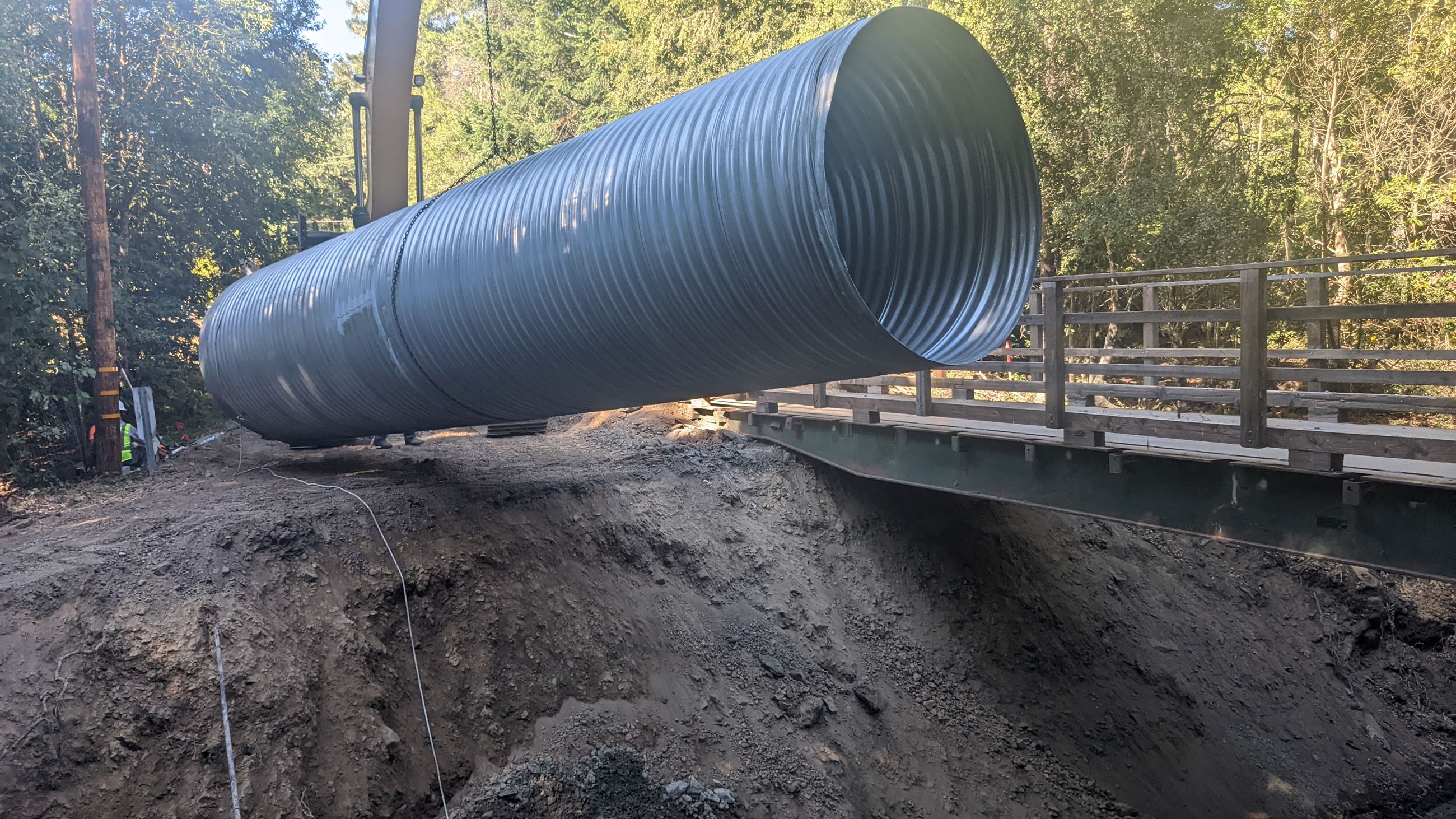 An excavator lifting a large metal culvert.