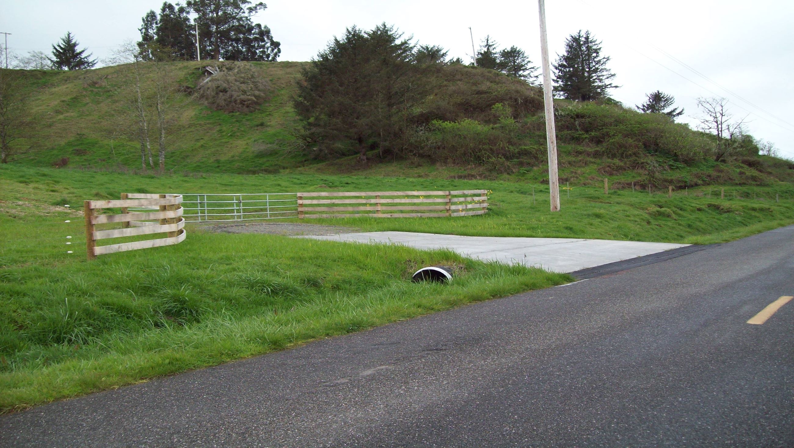 A newly paved driveway with a culvert connecting to a county road.
