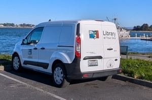 A small white van that has Library at Your Door & the Library's book logo on van doors.