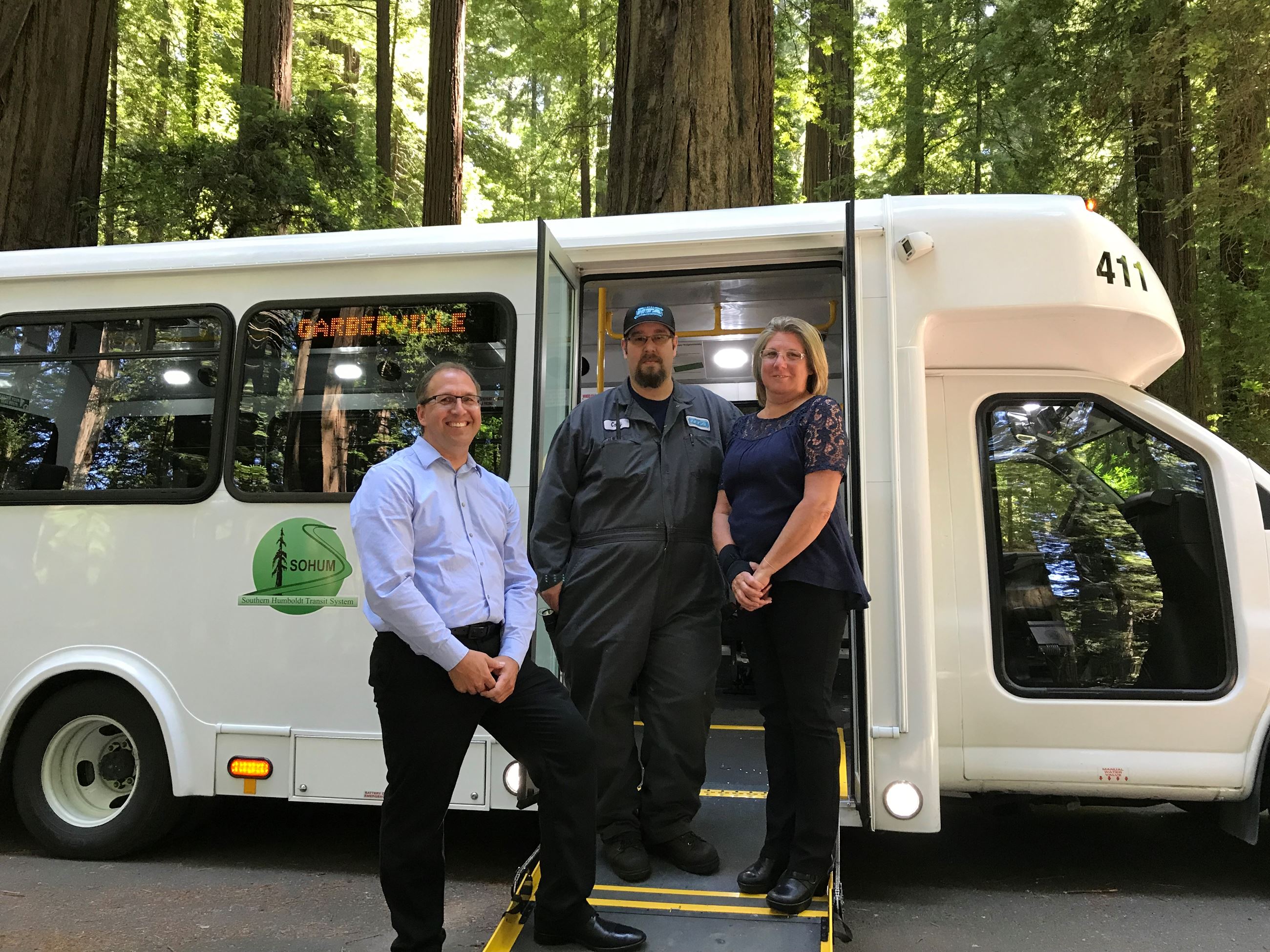 Humboldt Transit Authority bus with three staffers standing in front of it. Tree from the Avenue of 