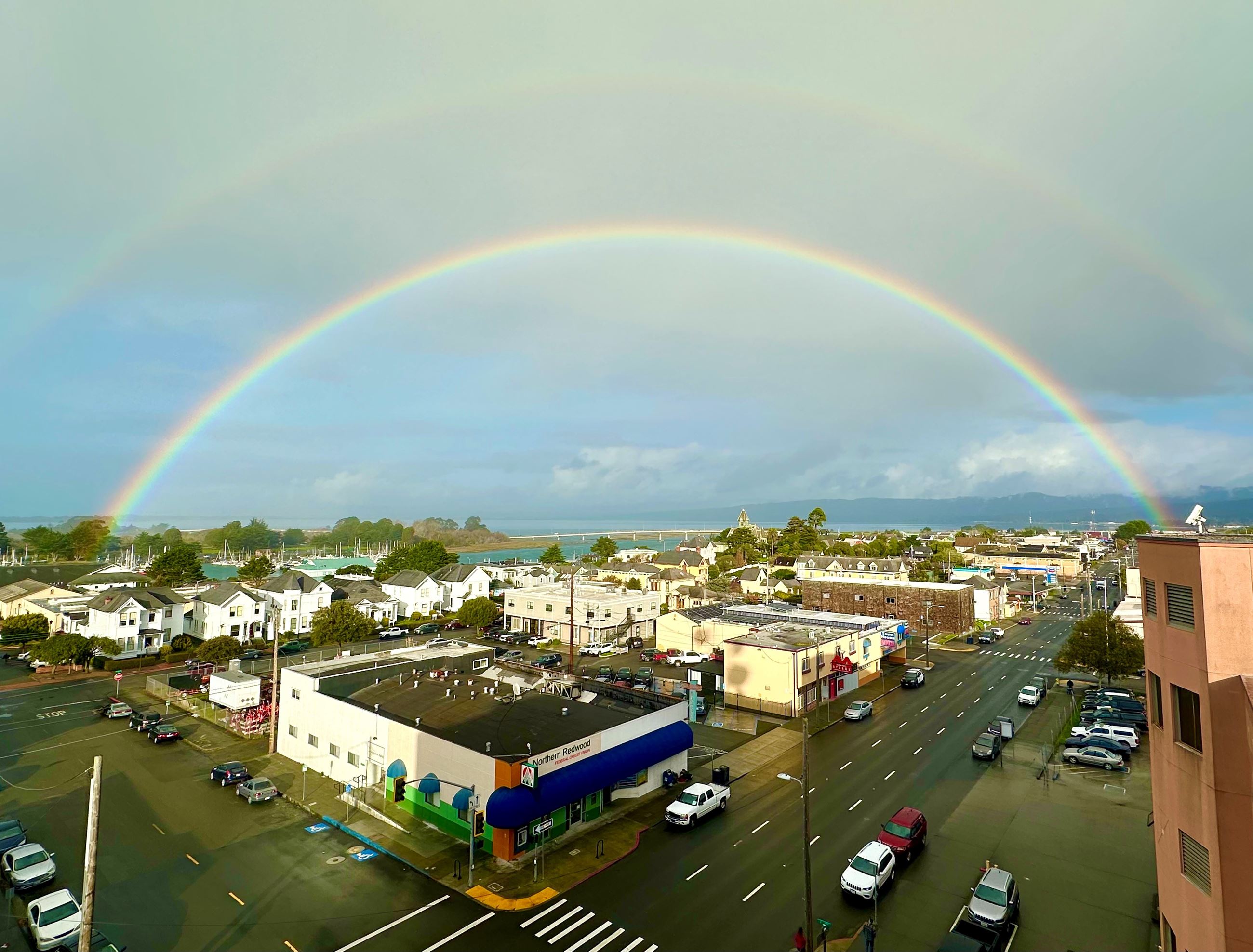Aerial view of downtown Eureka with a bright double rainbow spanning the sky above wet streets and buildings.