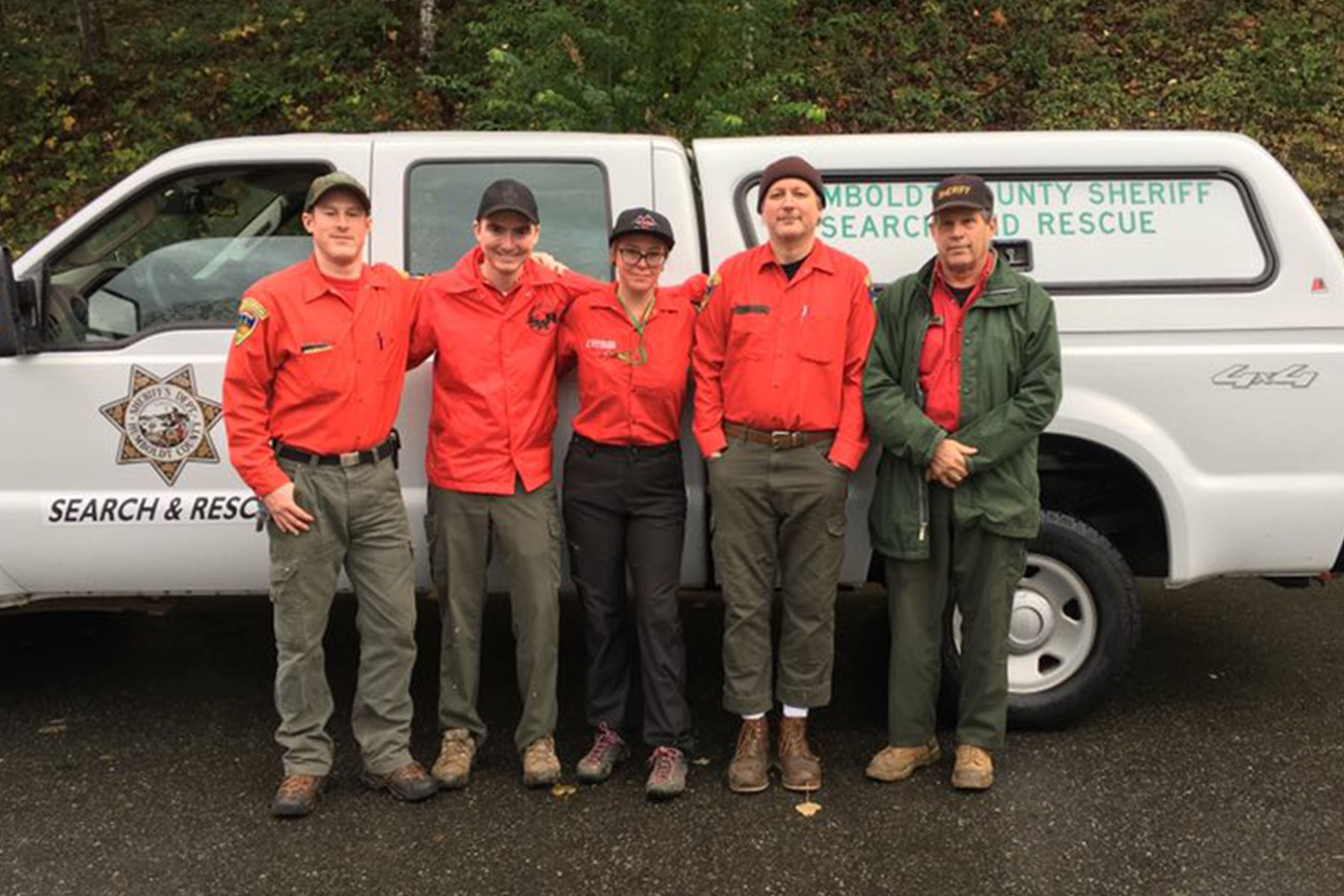 Five search and rescue members stand in front of a truck Opens in new window